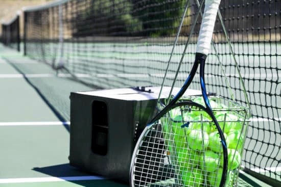 tennis balls in a basket next to a tennis racket